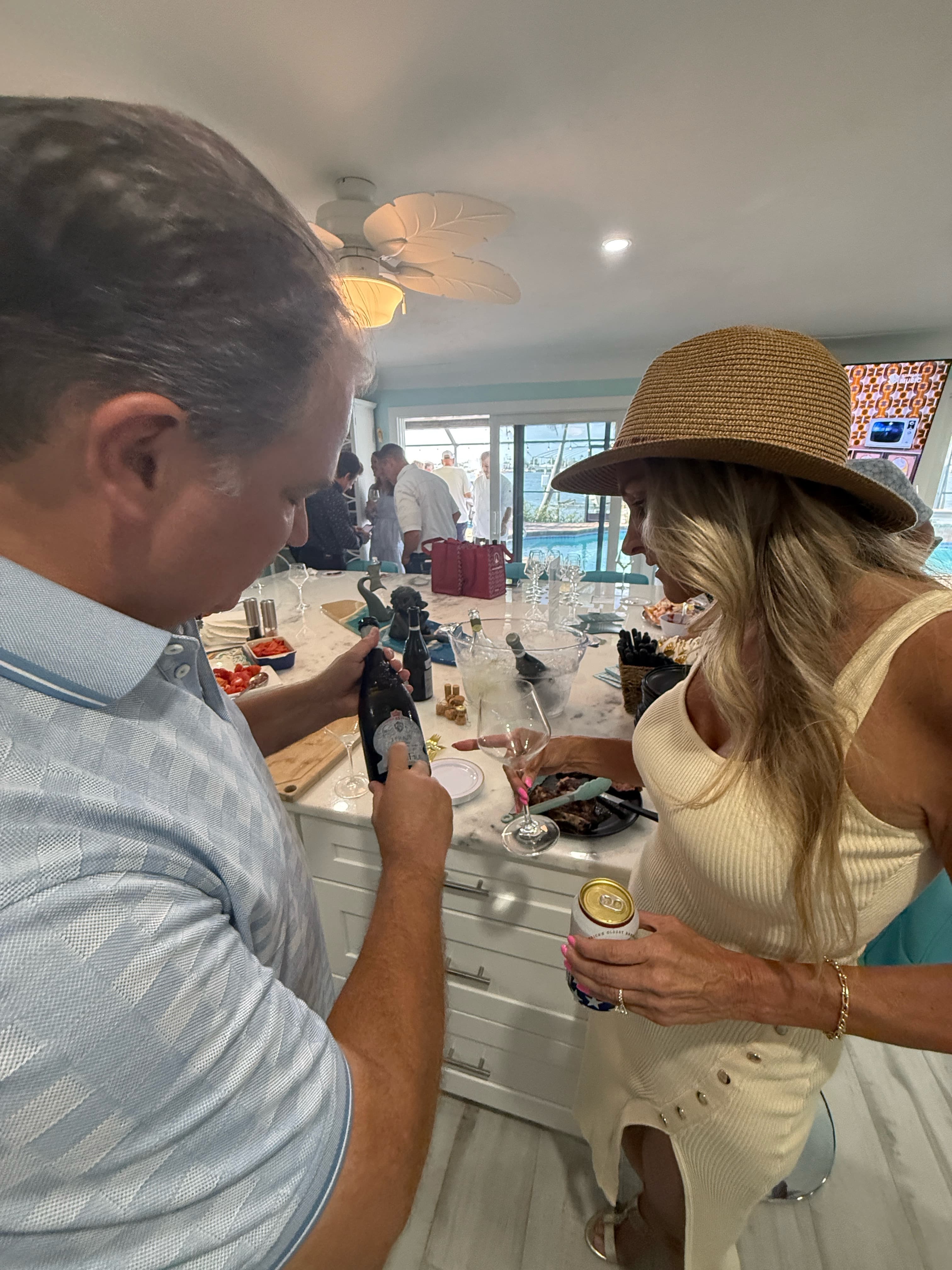 Man in blue shirt and woman in straw hat preparing drinks at a kitchen counter.